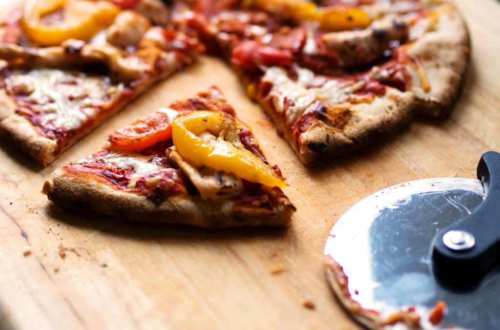 Foto di una fetta di pizza tagliata da una pizza intera che si intravede