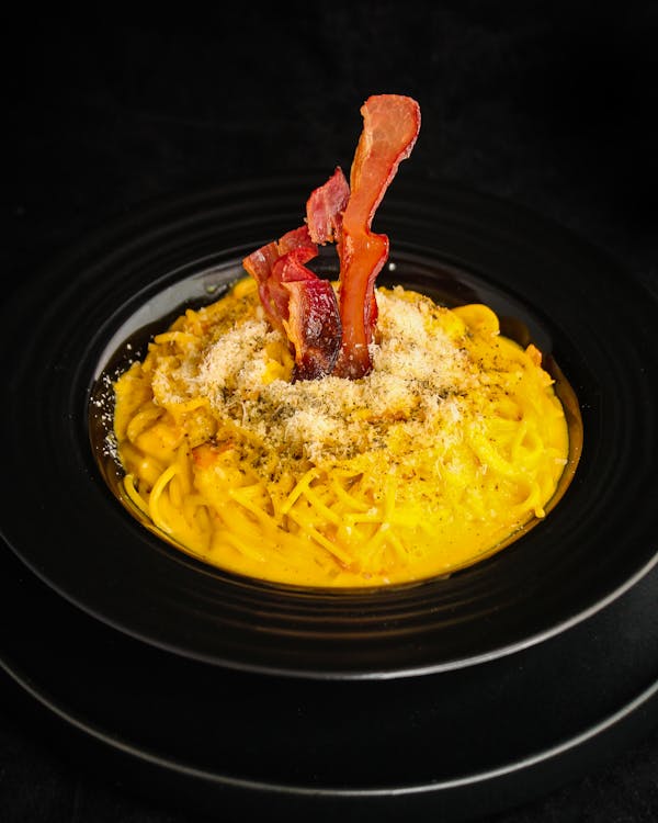 Foto di un piatto di pasta alla carbonara su un piatto nere e sfondo nero