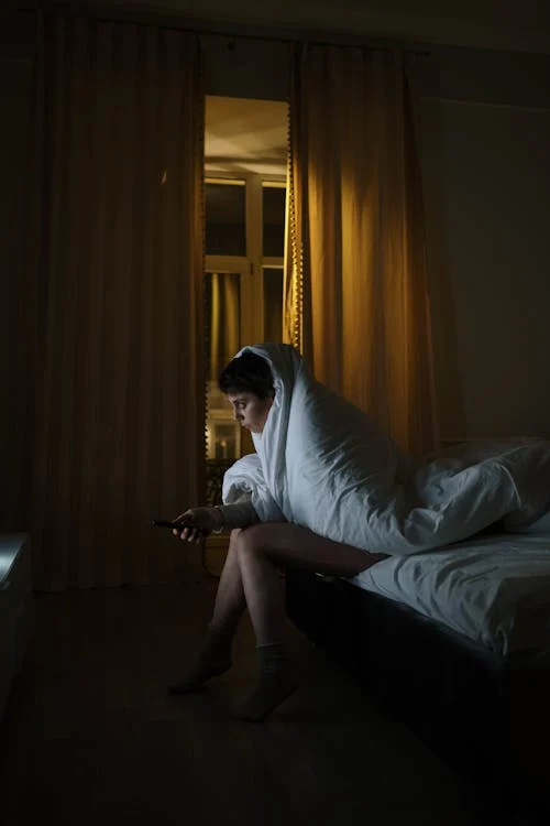 Foto di una persona ai piedi del letto con la coperta avvolta sopra ed in mano un telecomando