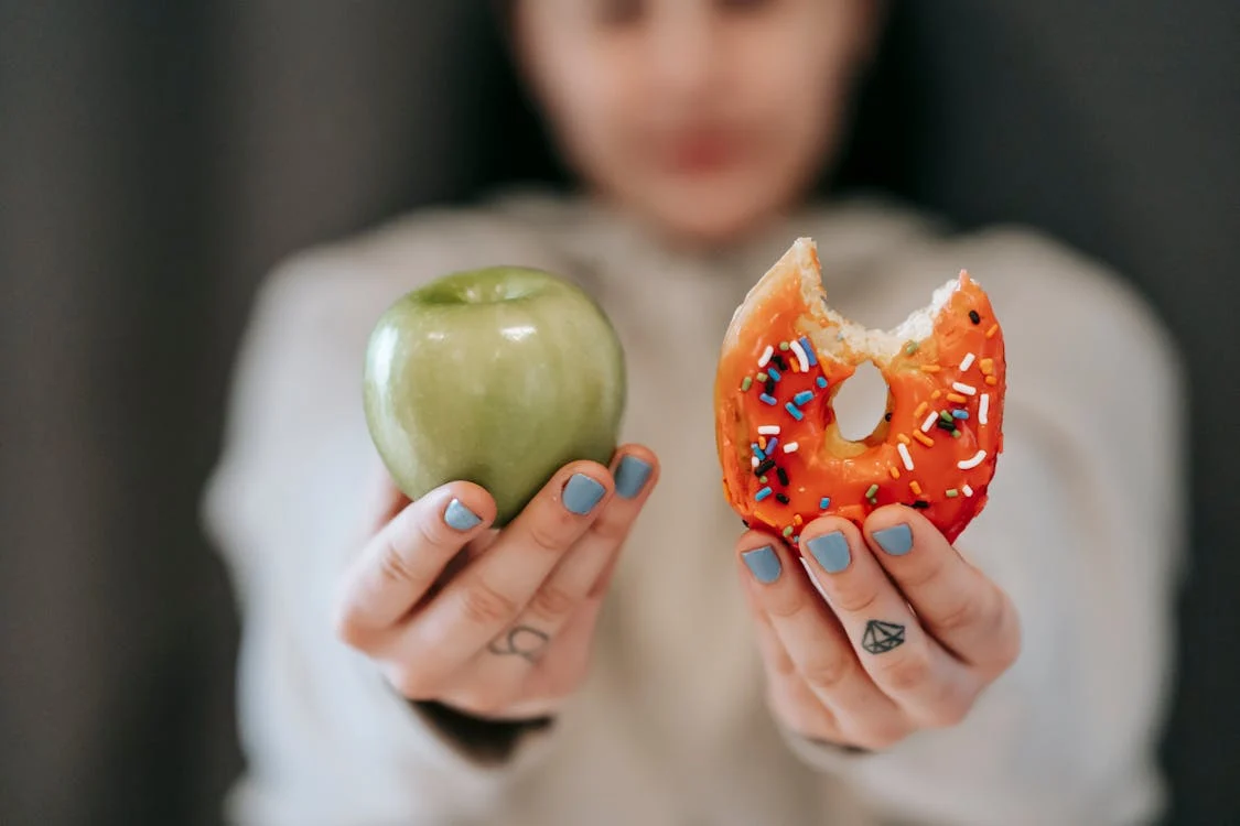 foto di due mani una regge una mela e l'altra una ciambella zuccherata