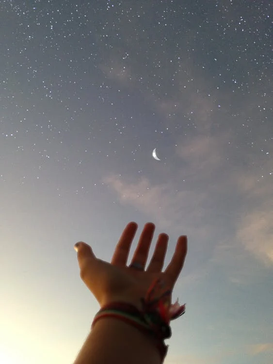 foto di una mano in prospettiva rivolta verso la luna nel cielo stellato