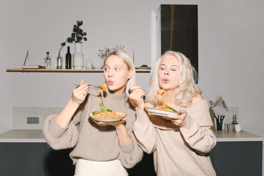 Foto di una donna e una ragazza che tengono in mano un piatto di spaghetti e mangiano in piedi