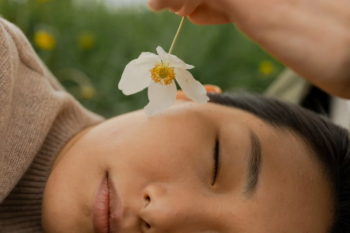 volto di una donna che dorme con una mano che le passa un fiore sulla guancia