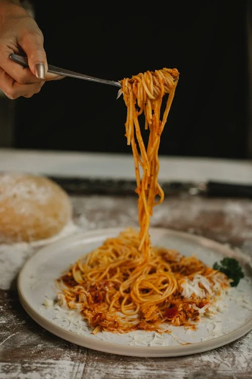 Foto di un piatto di spaghetti al pomodoro e una forchetta che li raccoglie