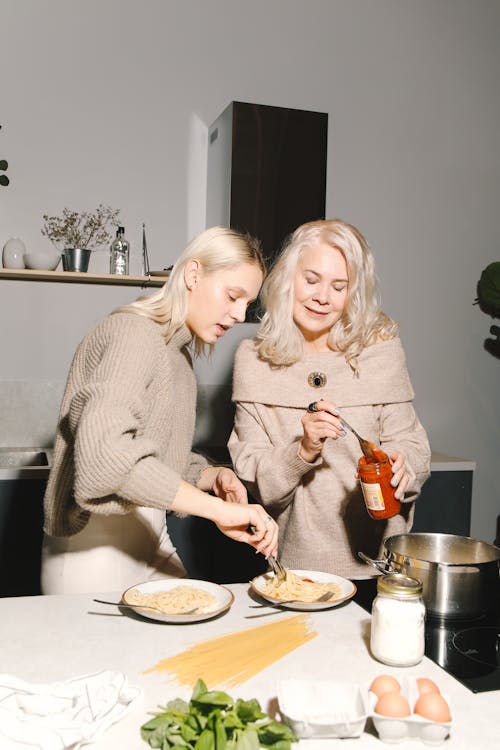 Foto di una donna e una ragazza che stanno in piedi in una cucina mentre preparano gli spaghetti 