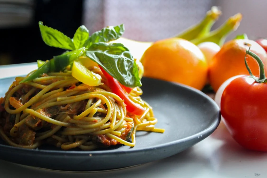 Piatto di spaghetti con del basilico sopra e dei pomodori vicino