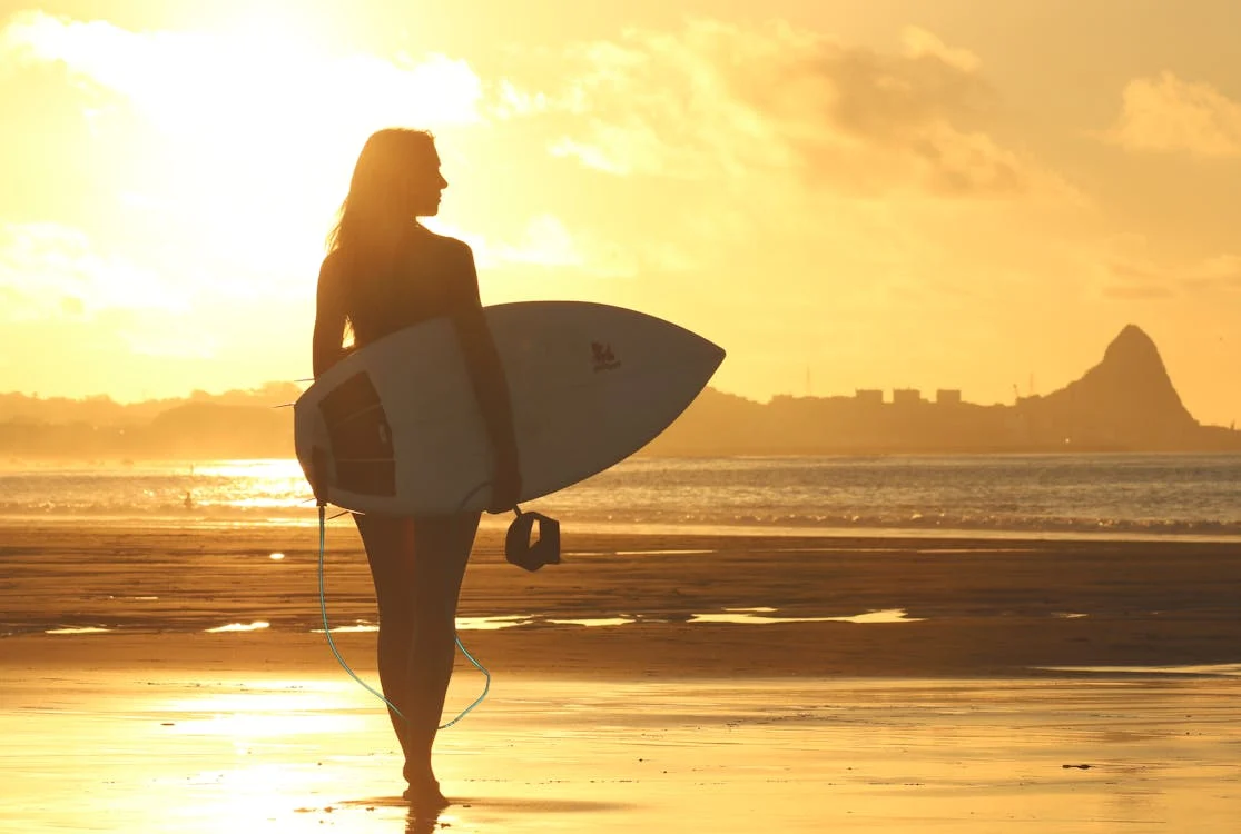 Foto di una ragazza mentre passeggia sulla spiaggia con la tavola da surf sotto braccio al tramonto