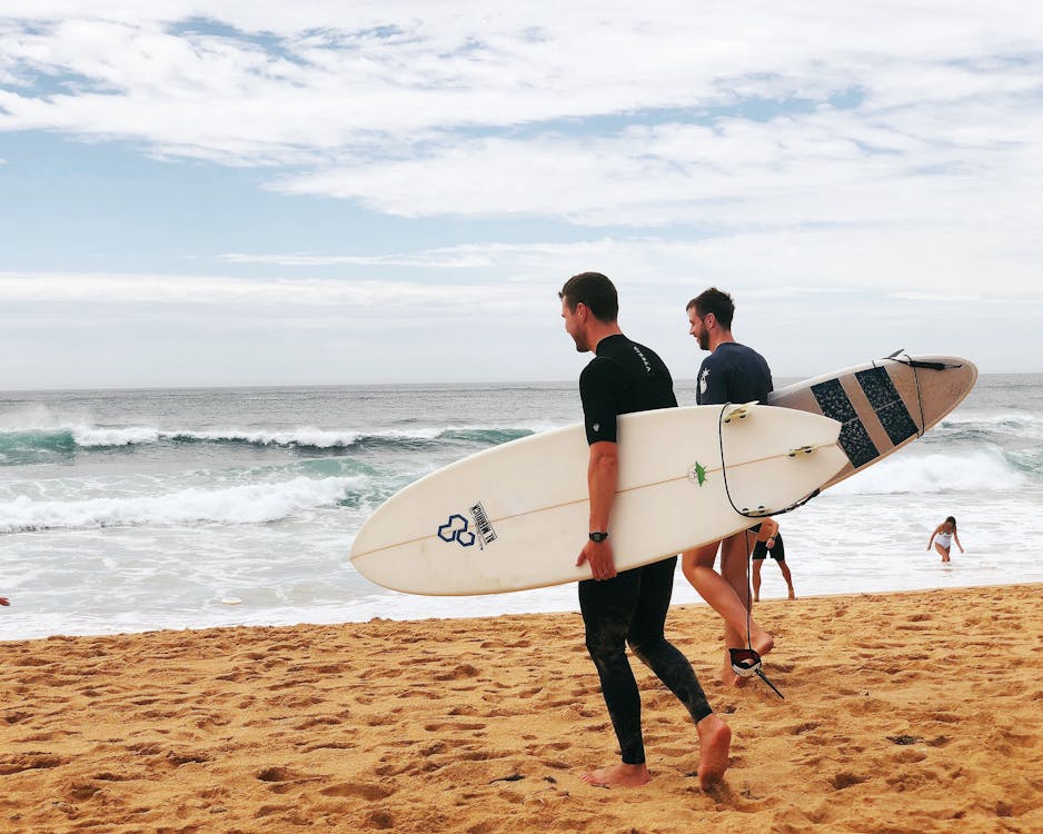 Foto di due ragazzi sulla spiaggia con la tavola da surf sotto braccio che si dirigono verso il mare