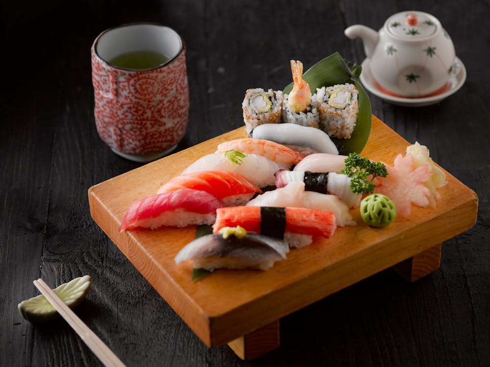 Foto di una tavoletta di legno con del sushi sopra e una tazza di tè vicino