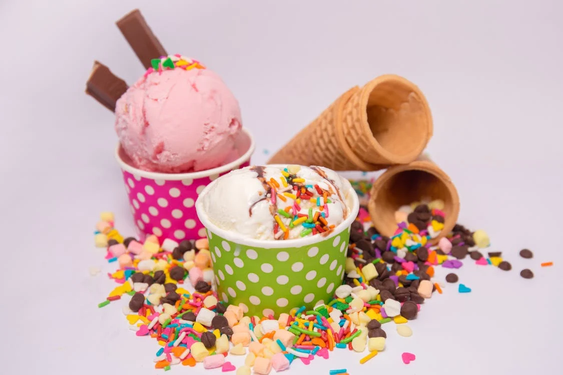 Foto di coppette di gelato colorate con dei coni vuoti accanto e dei zuccherini colorati sotto
