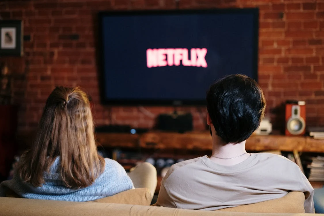 Foto di un ragazzo e una ragazza di spalle sul divano che guardano la tv